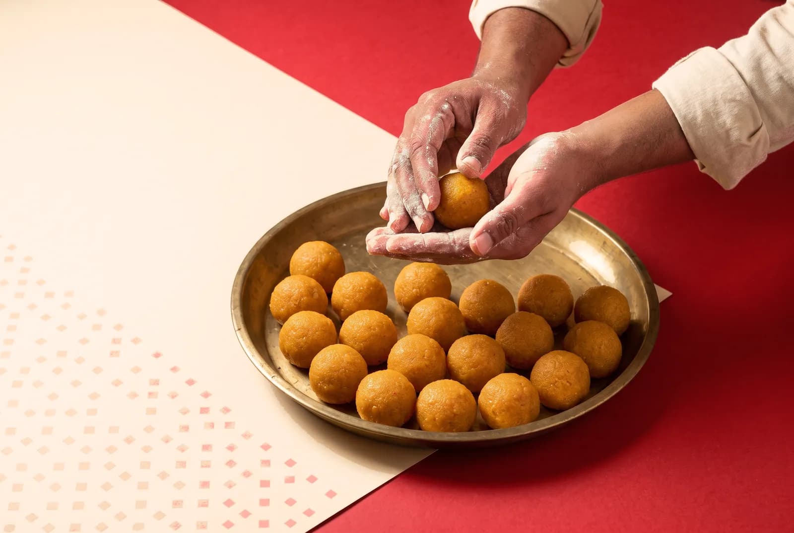 A sweet-maker rolling motichoor laddoos over a brass thali